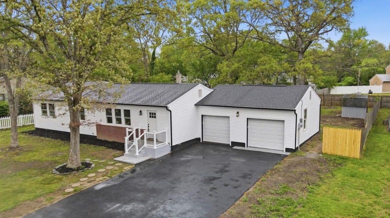 After: the same ranch house with new white siding, new roof, new garage doors and a fresh driveway