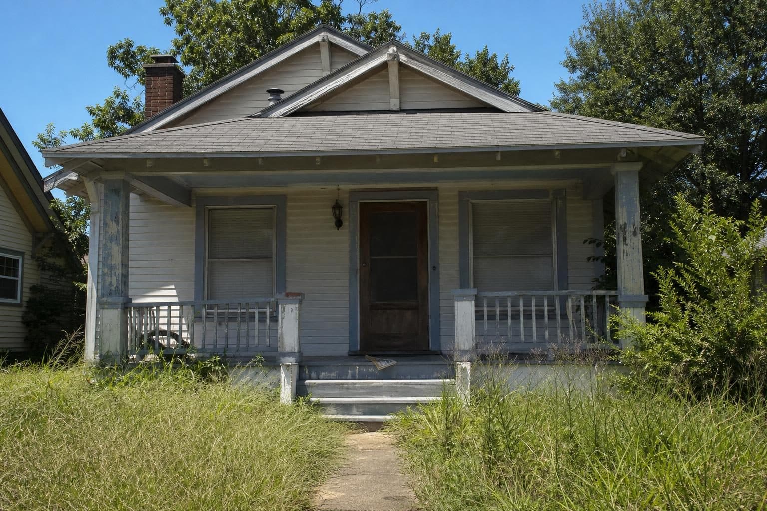 Vacant bungalow with knee-high grass and closed blinds